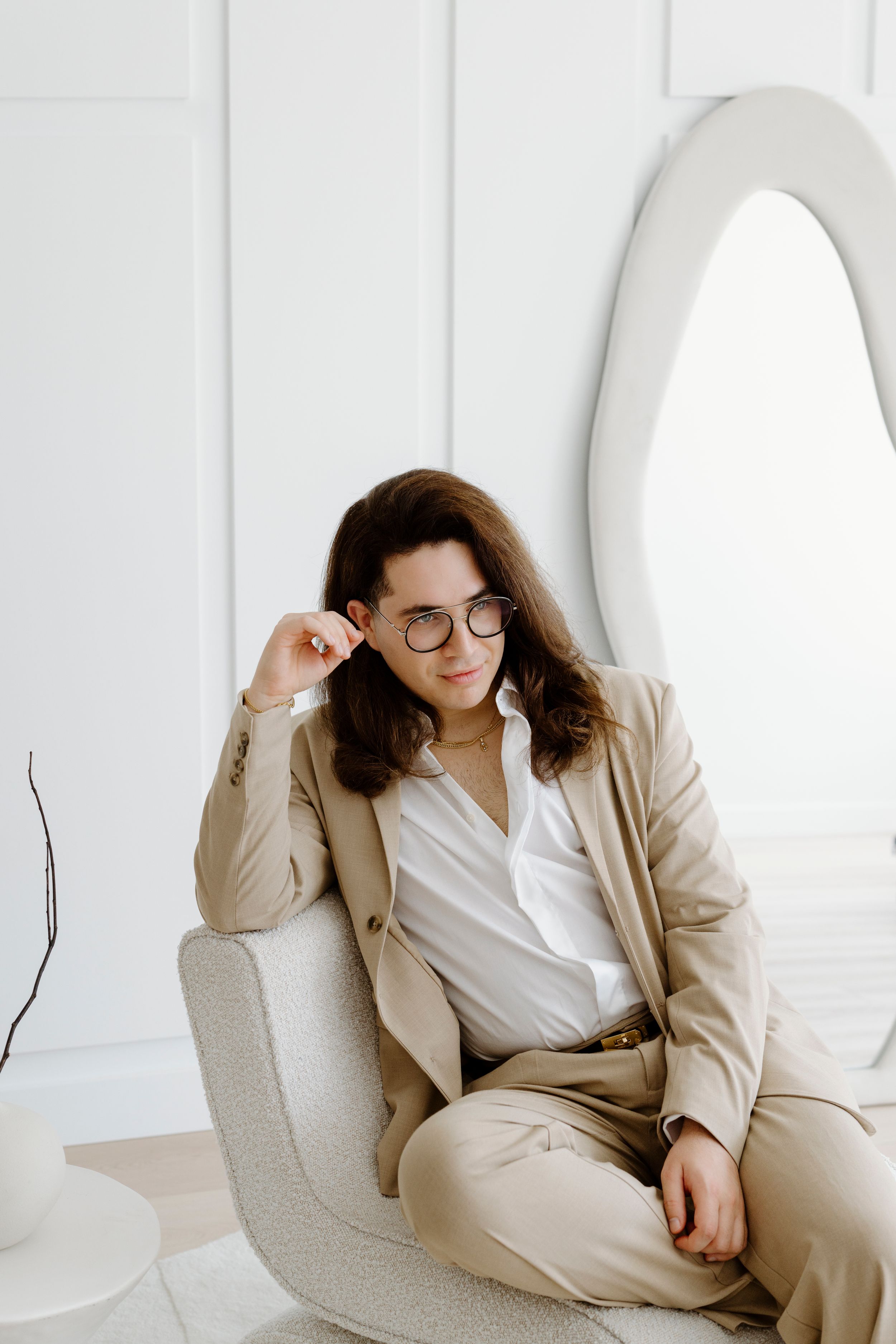 Professional wearing beige suit relaxes in modern white curved chair.
