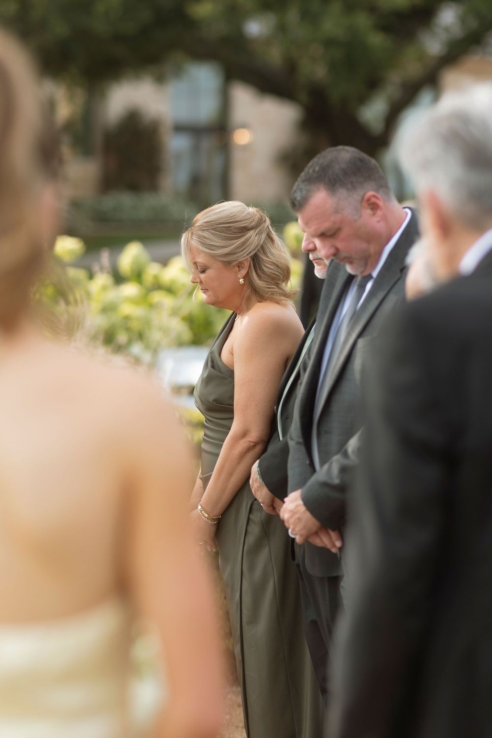 Wedding attendees in formal attire stand in rows during an outdoor ceremony.