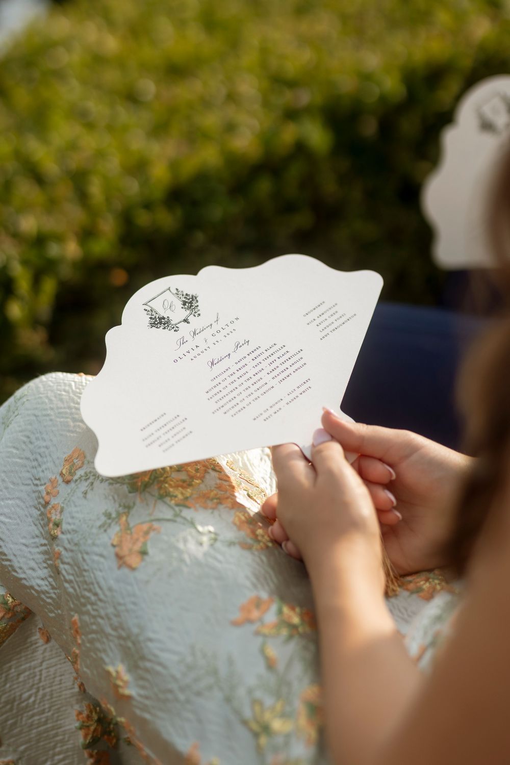 Hands holding and reading handwritten text on a textured white paper with golden accents in natural outdoor lighting.