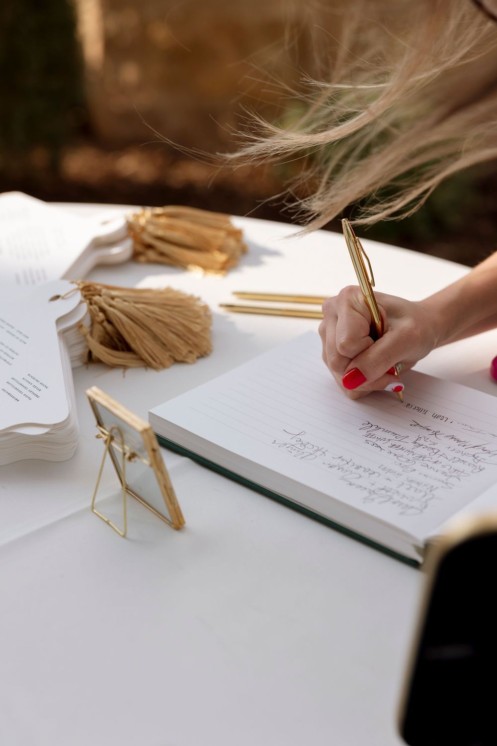Wedding guests signing a guestbook with decorative elements and pens on a white surface.