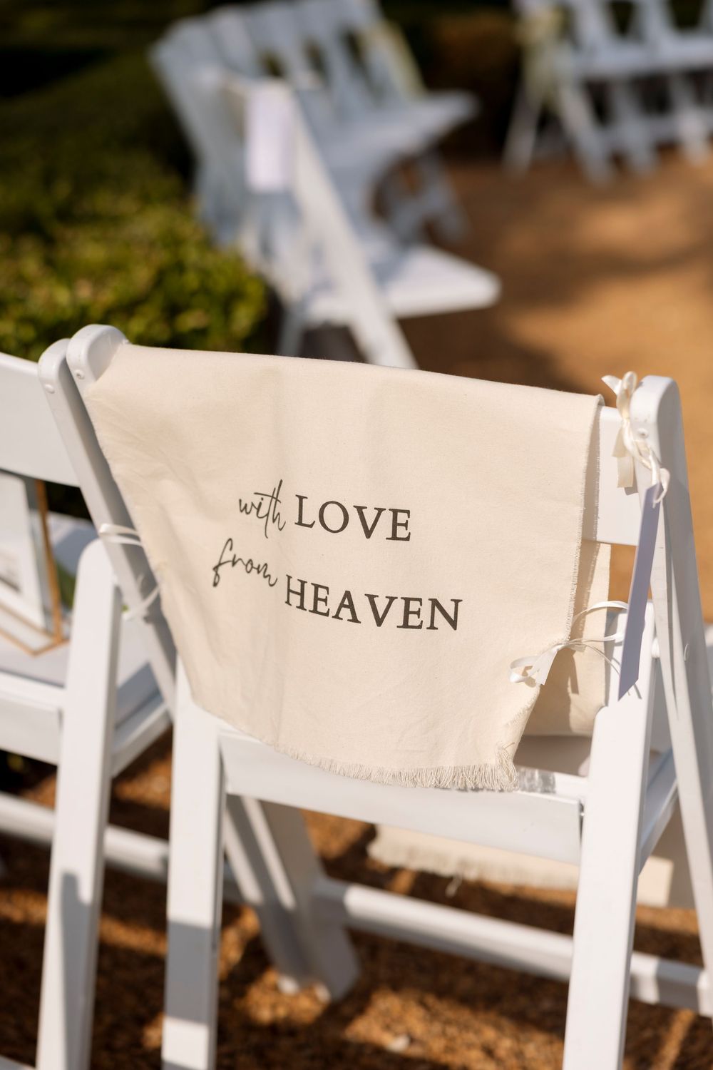 White wedding ceremony chair with a cloth sign reading 'with LOVE from HEAVEN' draped over the back.