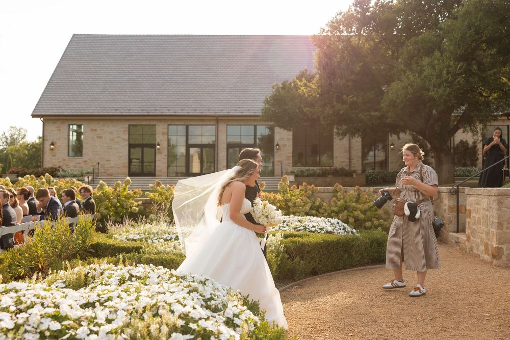 Outdoor wedding venue at sunset with stone buildings and garden landscaping visible in golden light.