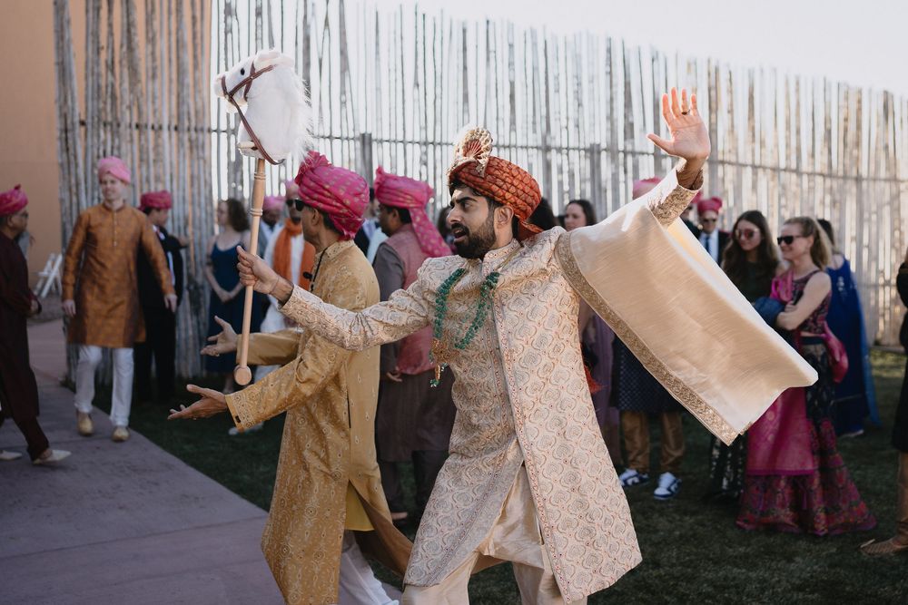 Groom in ivory sherwani and red turban dances joyfully with guests during a vibrant Indian Baraat procession.at Sandia Resort and Casino