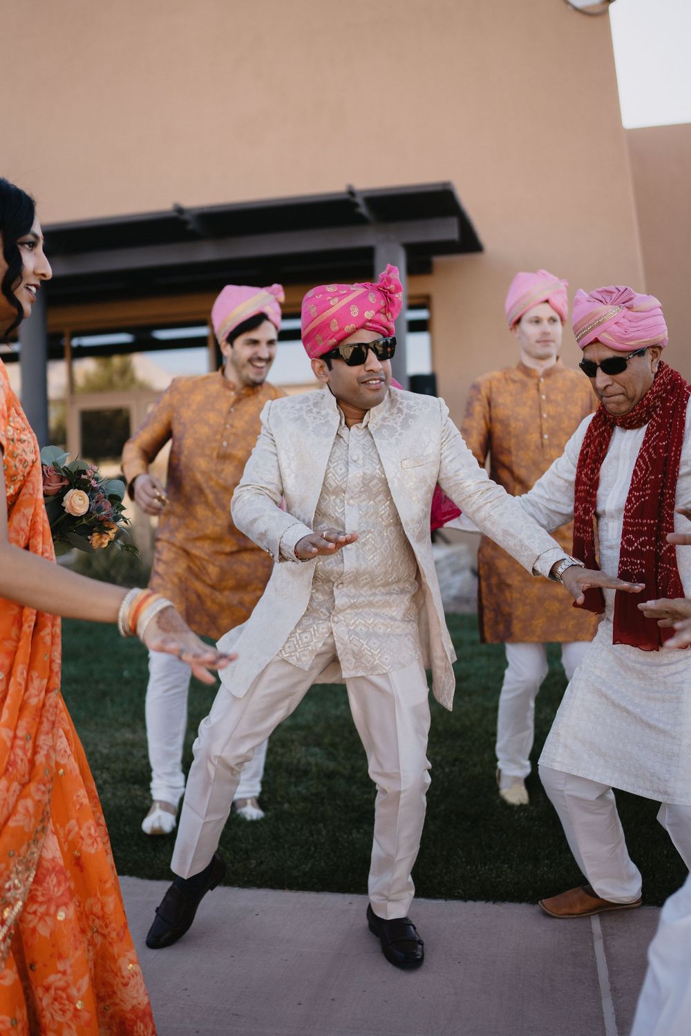 Groom in white sherwani dances energetically with groomsmen in orange kurtas and pink turbans at Indian wedding.at Sandia Resort and Casino