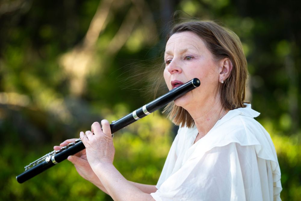 Someone in white ruffled clothing plays a flute in a sunlit outdoor setting.