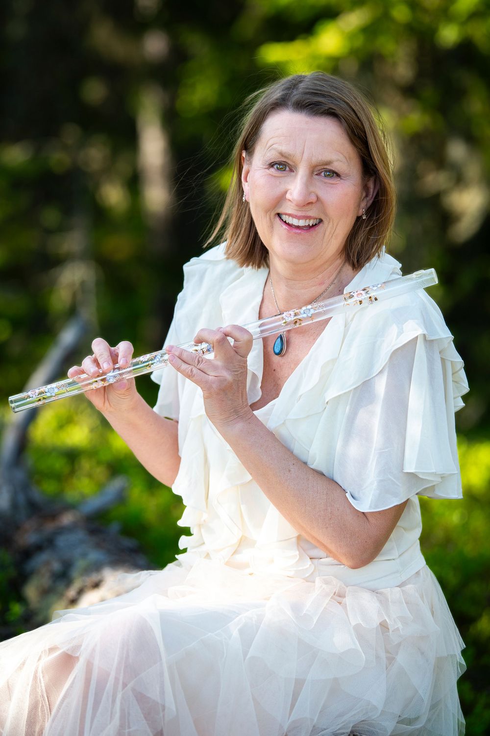 A musician in a white ruffled dress performs with a flute in a garden setting.