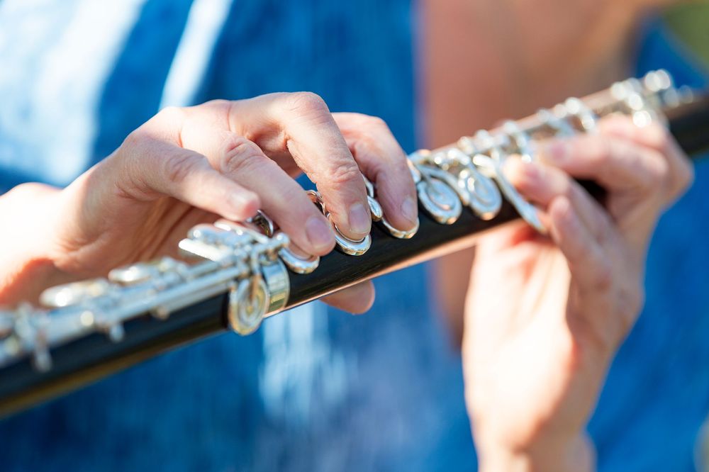 Close-up details of hands playing a silver flute with precise finger positioning.