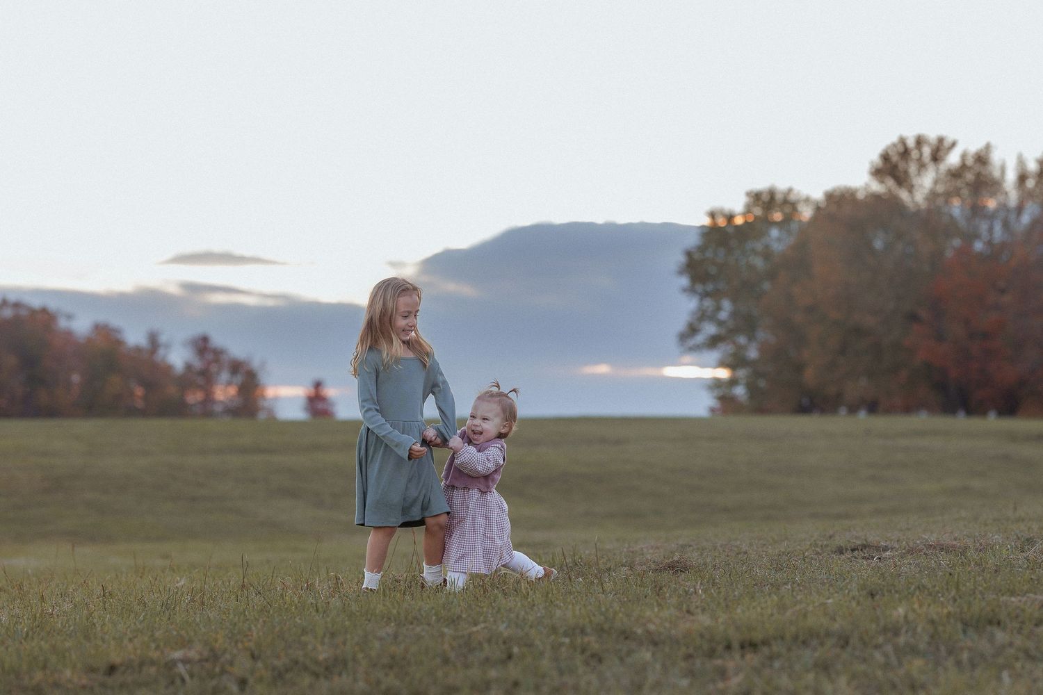 Children playing in a grassy field during golden hour with mountains in the background.
