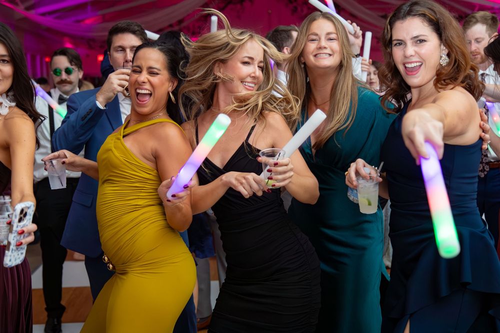 Party guests dancing with colorful light-up sticks at an evening celebration event.