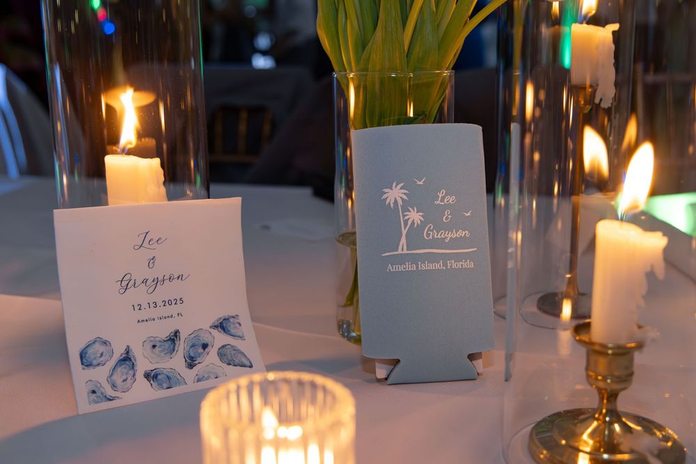 Wedding reception table setting with candlelight, seating cards and palm tree themed drink koozies.