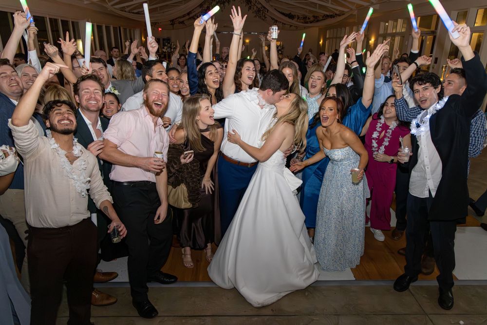 Wedding guests dance and celebrate on a rustic wooden dance floor during a lively reception party.