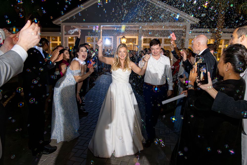 Newlyweds celebrate on dance floor under falling confetti at outdoor reception venue with clear tent.