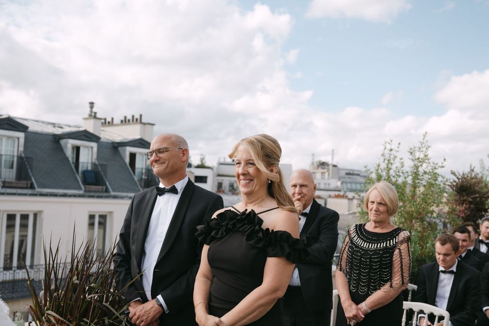 Wedding party gathers on an outdoor terrace for formal group photos on a sunny afternoon.