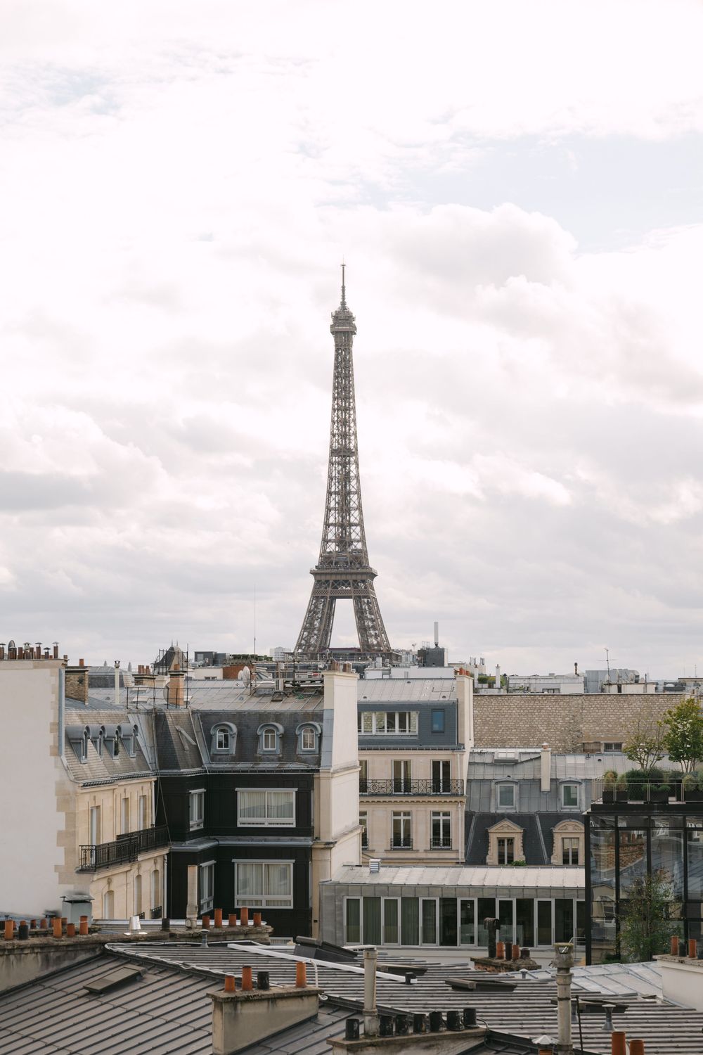 Panoramic view of Paris rooftops with the iconic Eiffel Tower visible in the distance on a cloudy day.