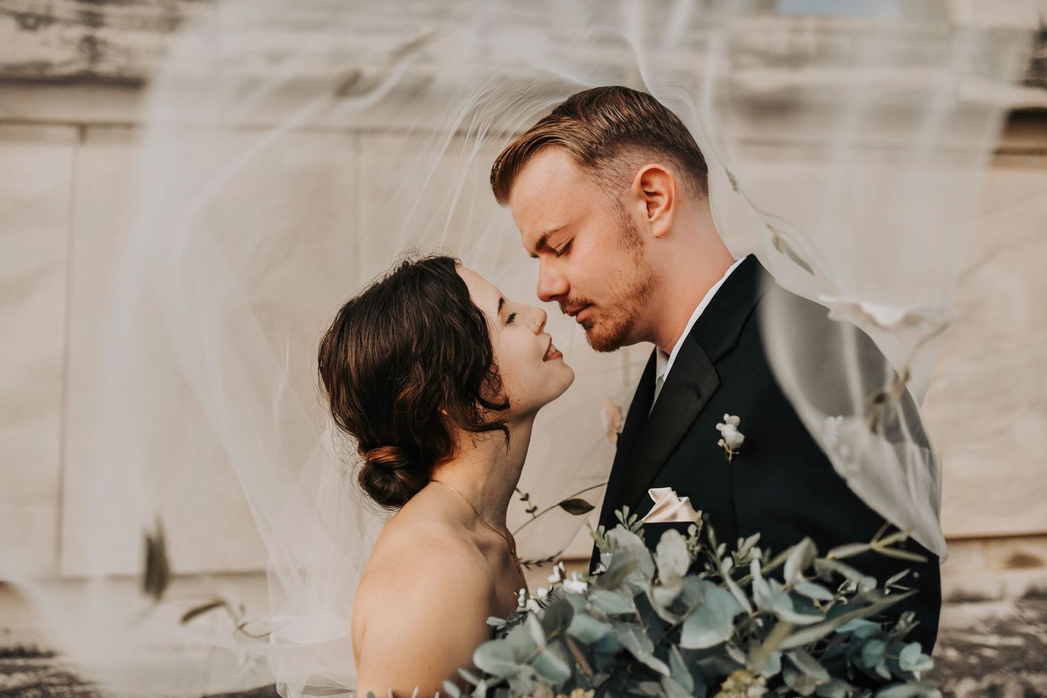 Bride and groom kissing under the veil during romantic wedding portraits at golden hour