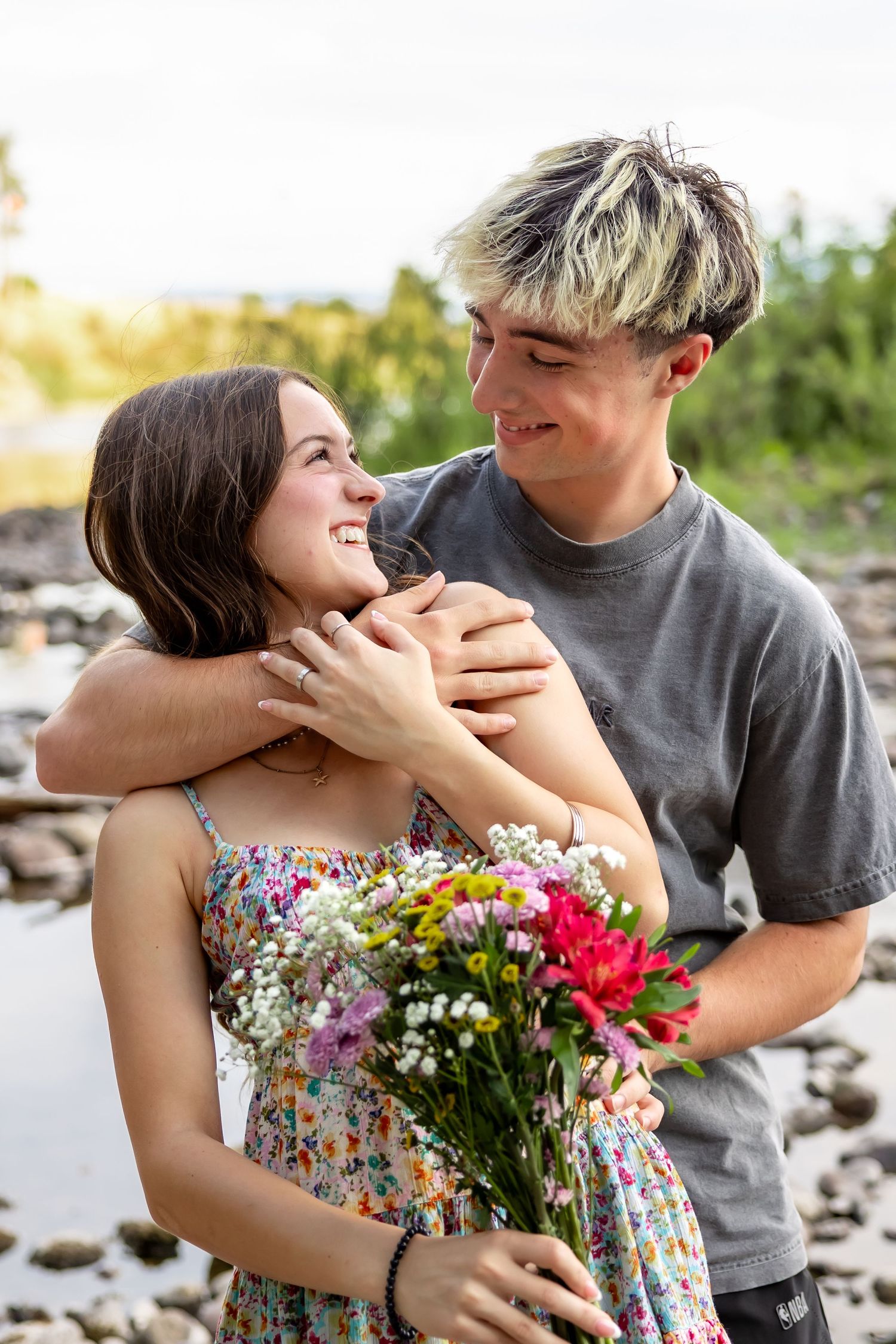 A romantic outdoor photoshoot with a couple holding a colorful bouquet of flowers in a natural setting.