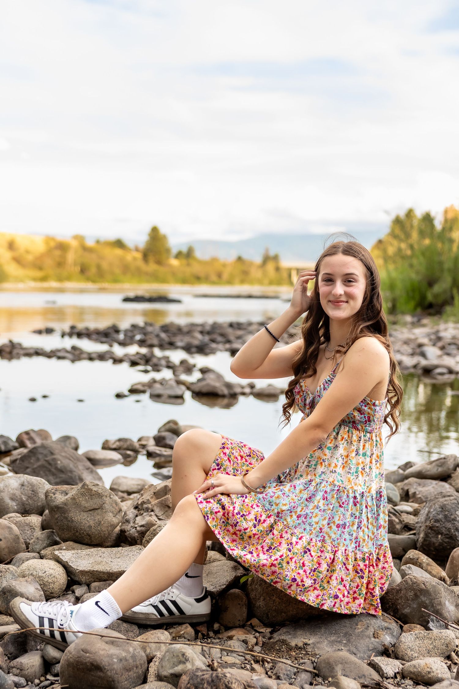 Someone in a floral dress and sneakers reclines on rocky shoreline during golden hour.
