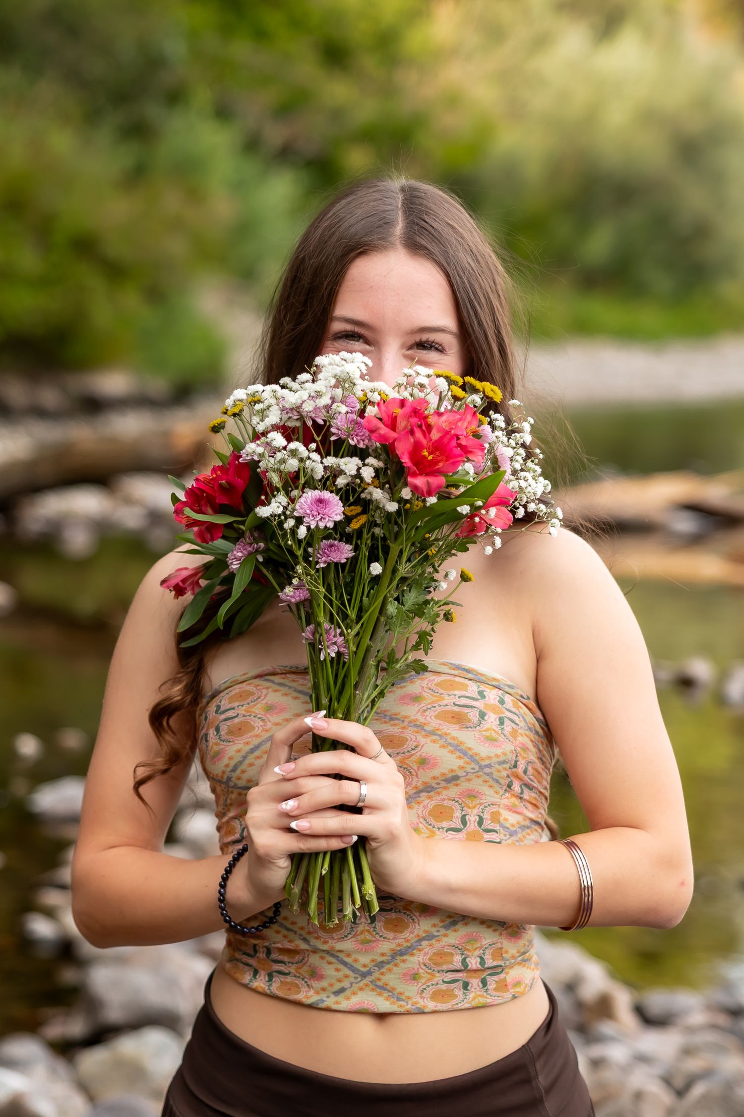 A bouquet of pink and red flowers held against a floral dress with a natural outdoor background.