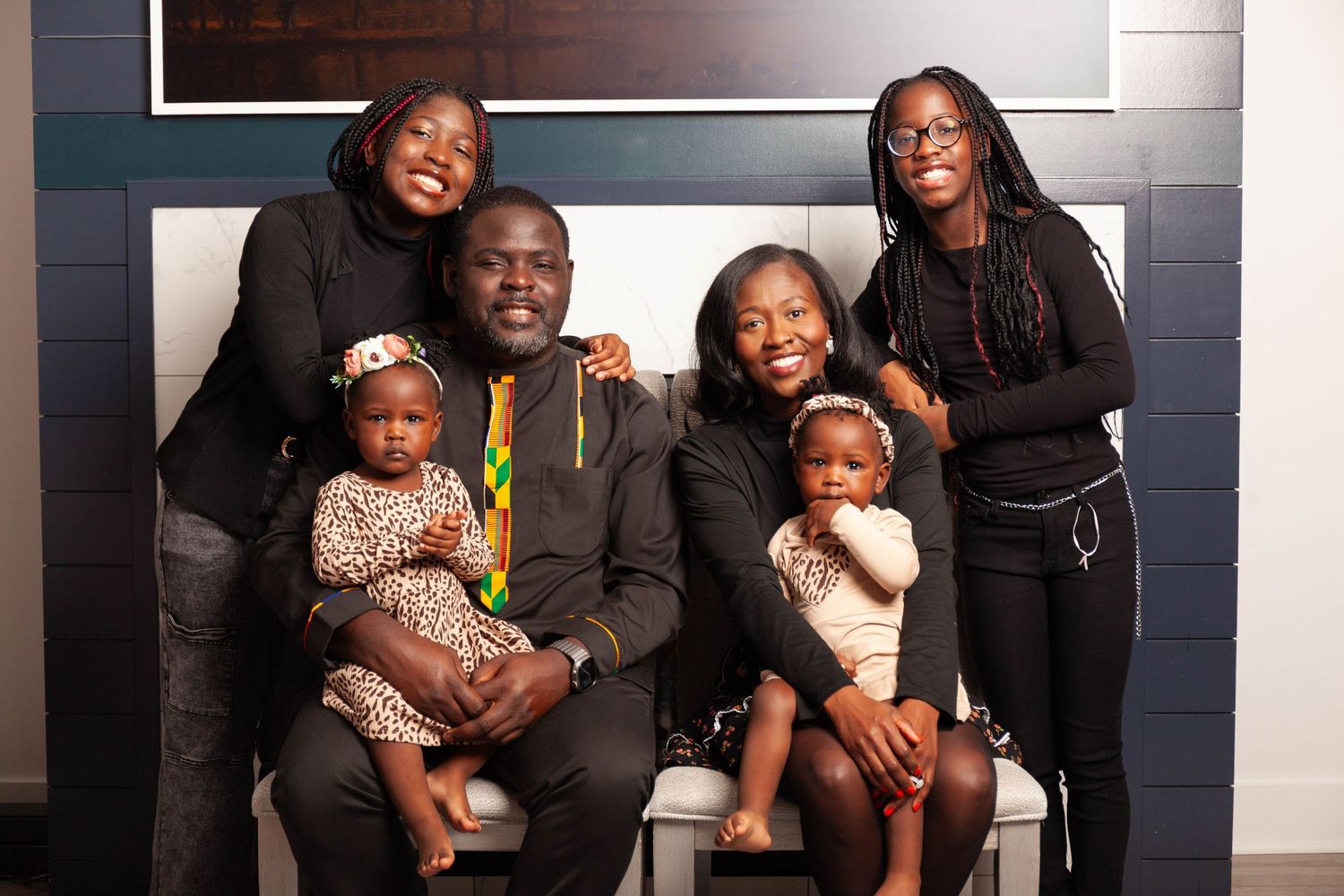 A family group poses together against a blue wall in a studio setting, wearing coordinated outfits.