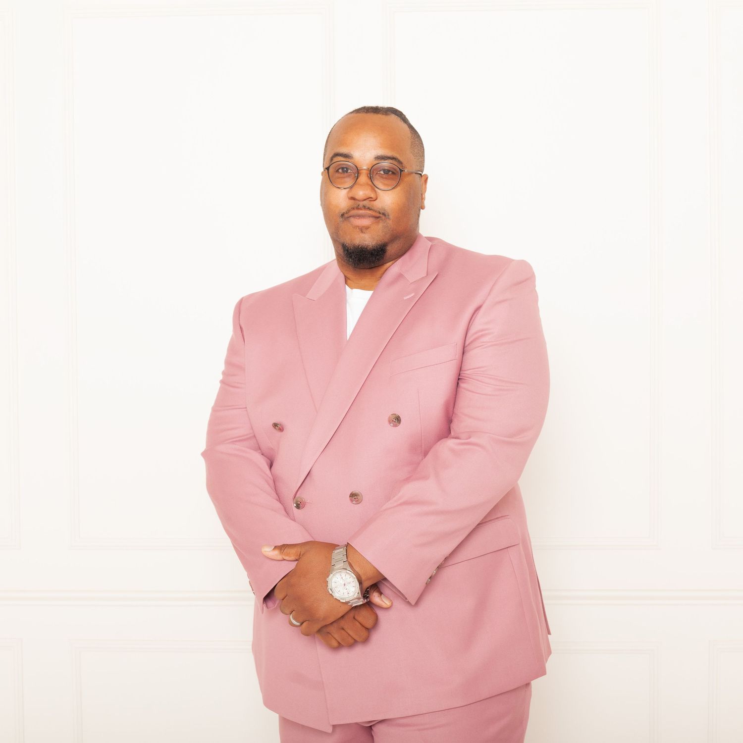 Professional wearing a stylish pink double-breasted suit jacket poses against a white backdrop.