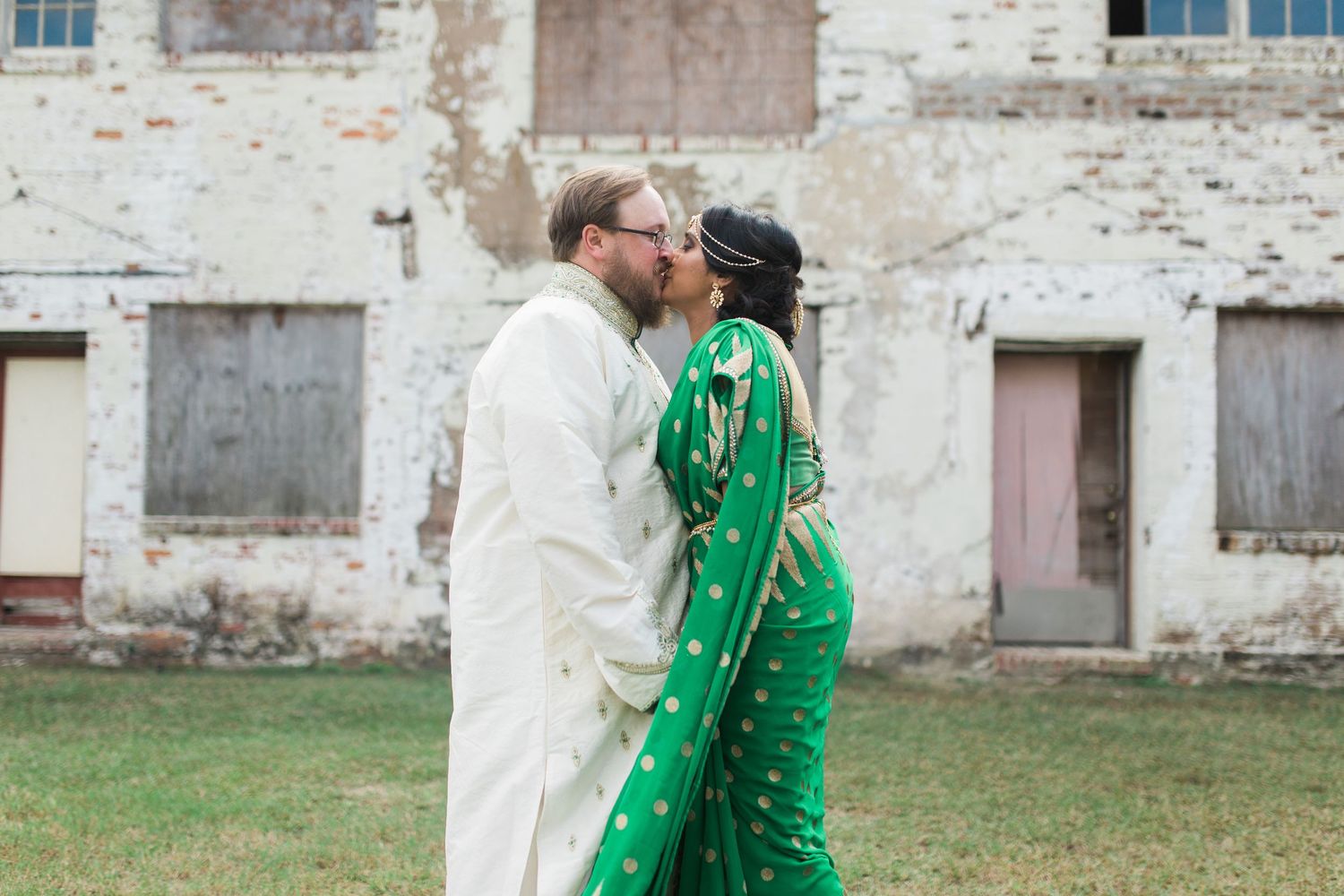 A couple shares an intimate moment against a rustic brick wall backdrop outdoors.