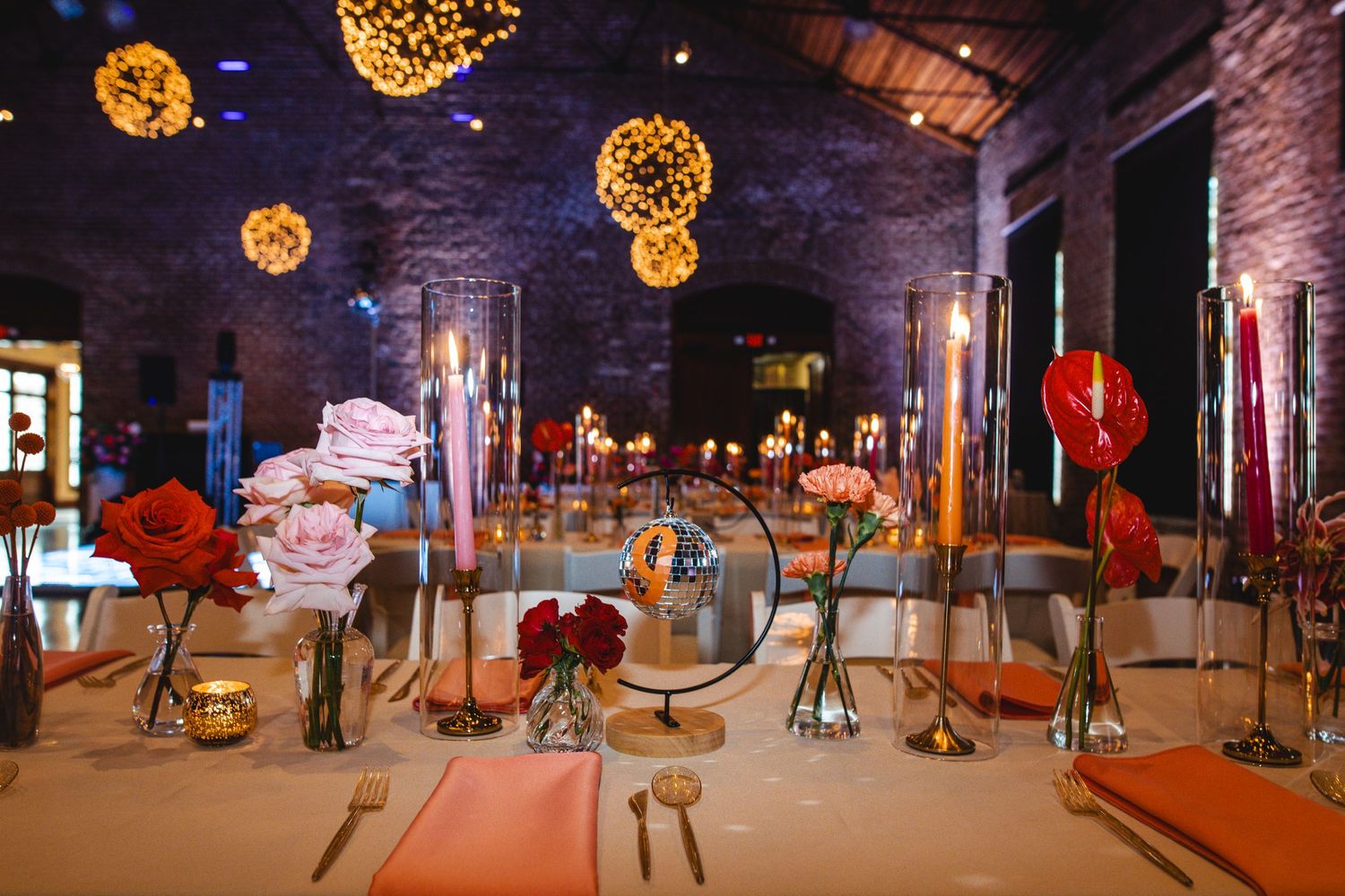 Elegant reception venue with glowing orb lights and red floral centerpieces in an industrial-style space.