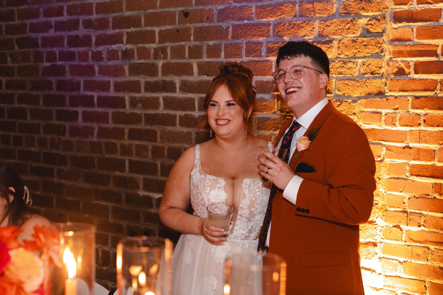 A couple shares their first dance at a wedding reception in a rustic brick-walled venue with warm lighting.