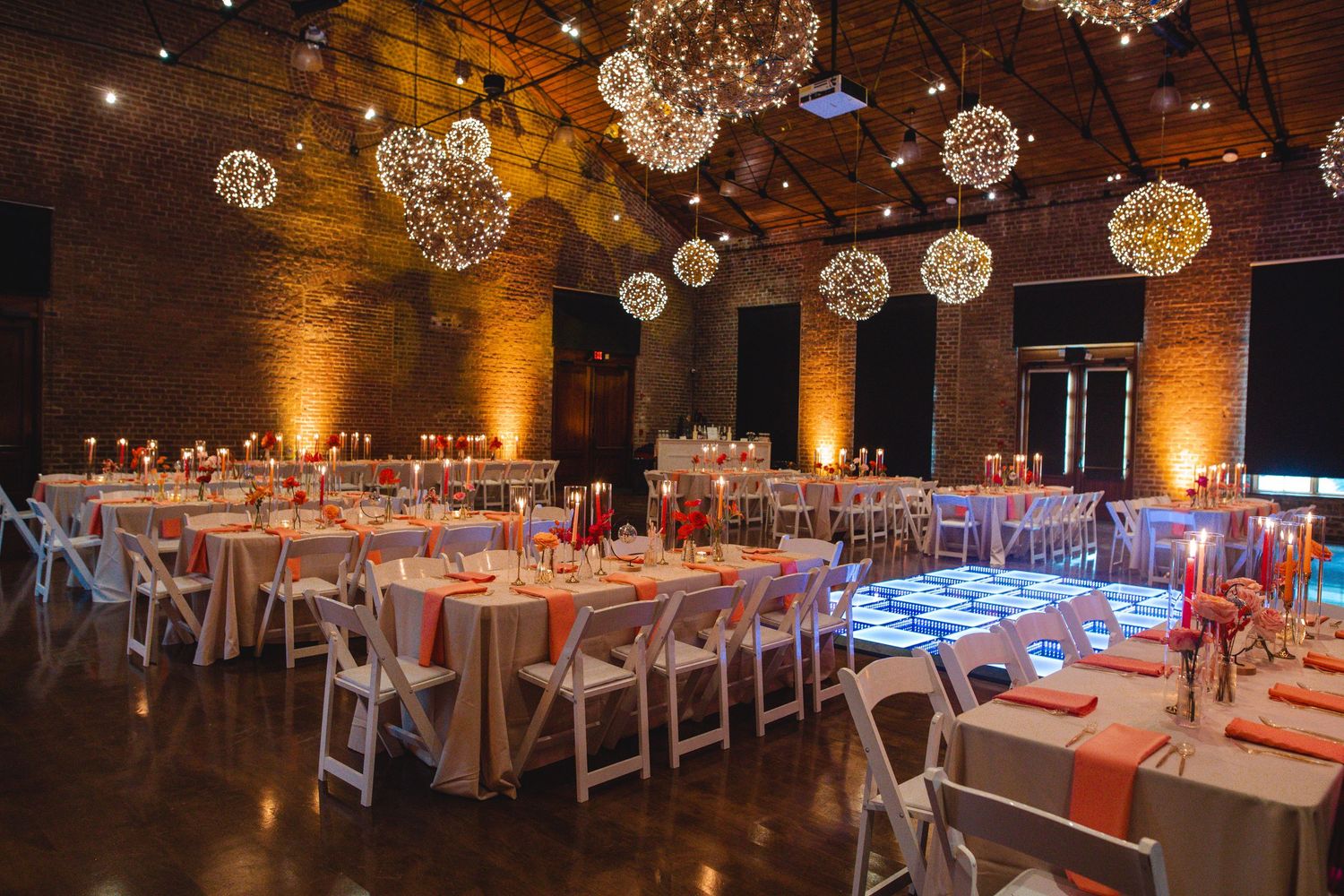 Elegant wedding reception venue with crystal ball light fixtures and long dining tables set with coral accents.