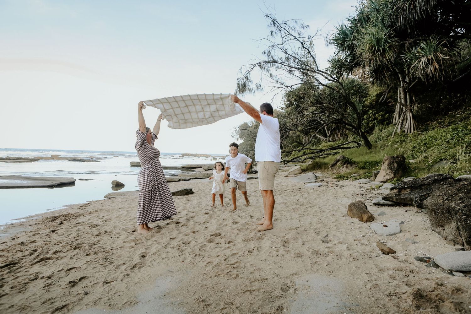 Family enjoying a relaxing walk together on a scenic beach with lush greenery and ocean views in the background.