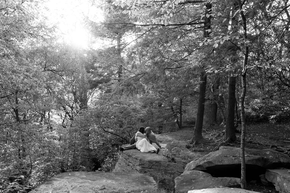 Black and white photo of a couple sitting on rocks in a sunlit forest.
