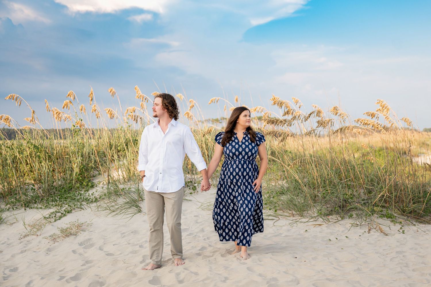 Couple strolling along beach path with golden sea oats in the background.