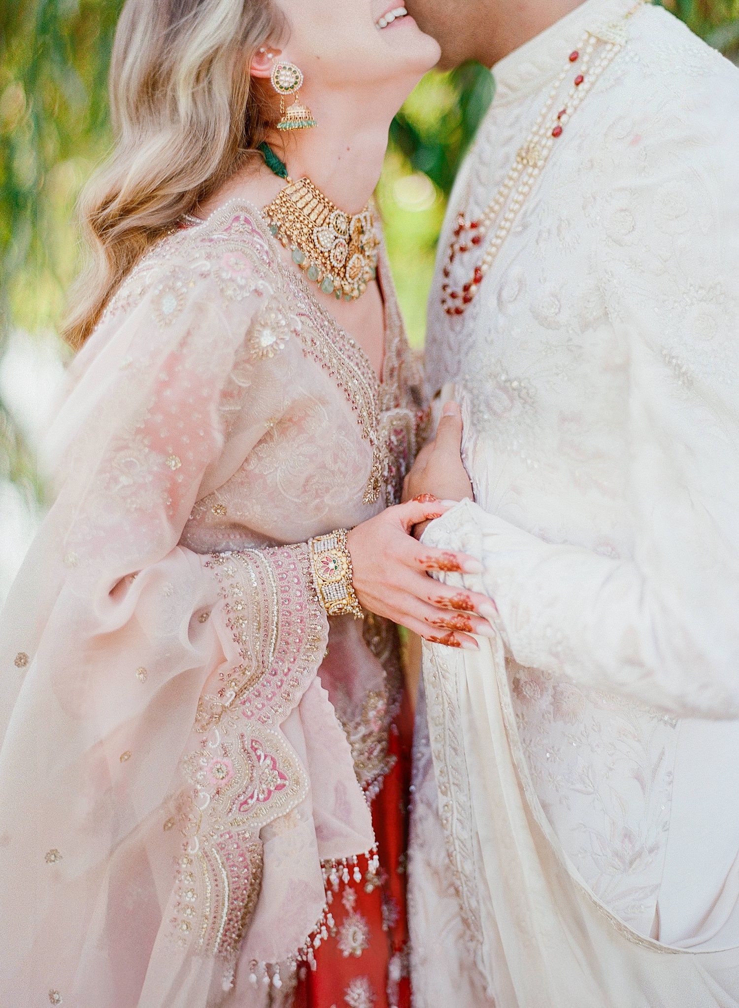 Couple in traditional South Asian wedding attire embracing in a romantic outdoor photoshoot with pink and white outfits.