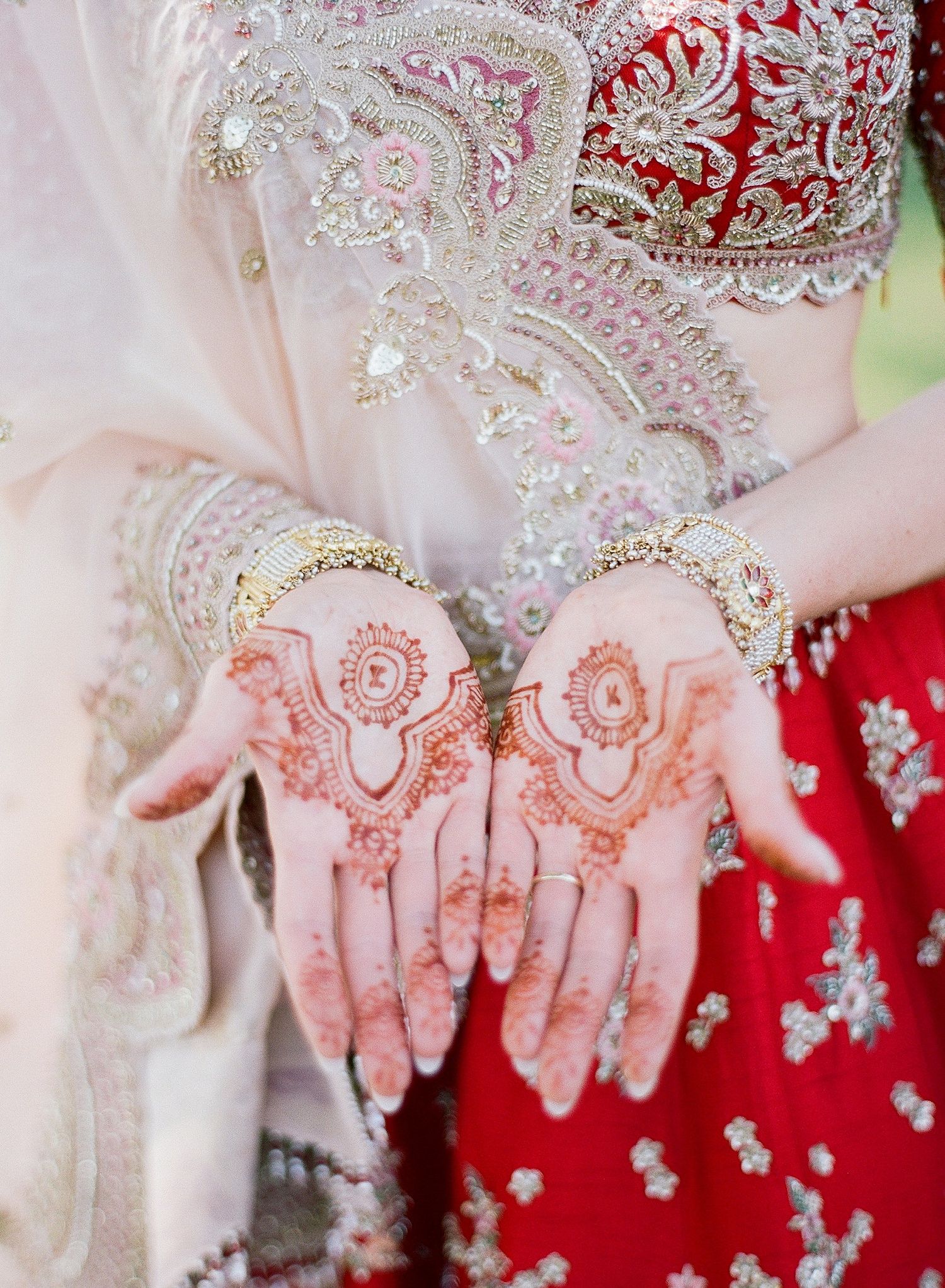 Intricate henna designs adorn hands against a backdrop of red and white traditional wedding attire.