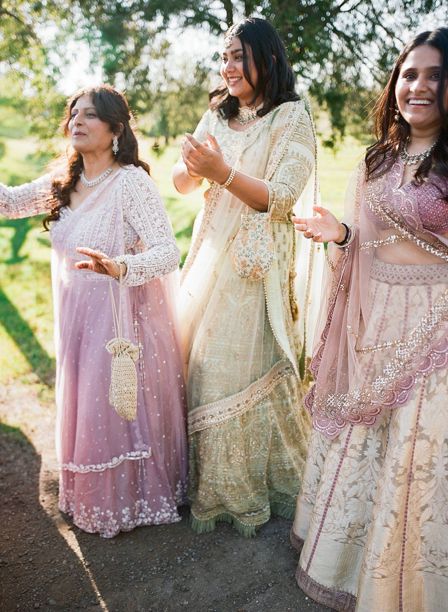 Friends in elegant pink and cream traditional South Asian outfits laugh together during an outdoor photoshoot.