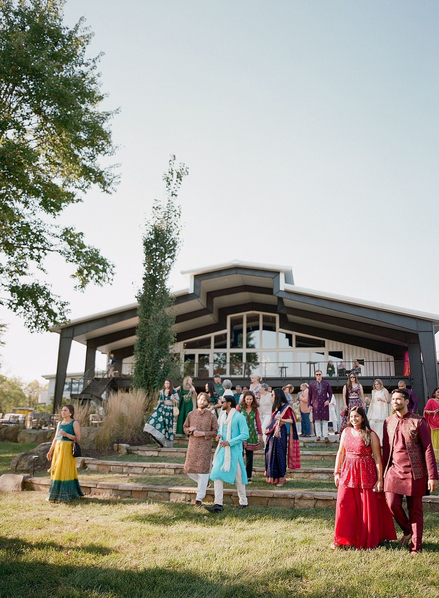 Wedding party gathers outside a modern architectural venue with sloped rooflines at sunset.