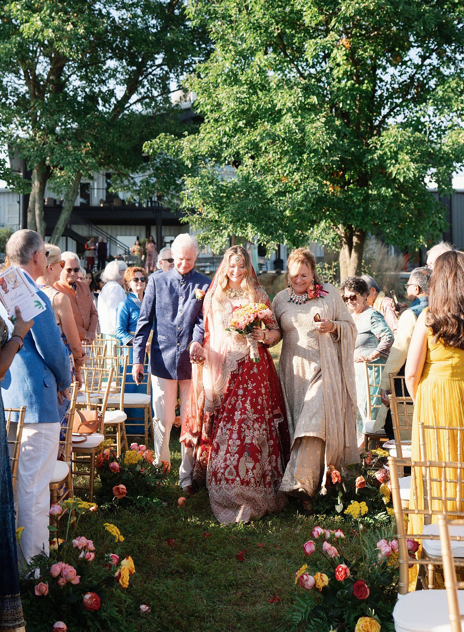Guests gather outdoors at a garden party event with pink flowers and trees in the background.