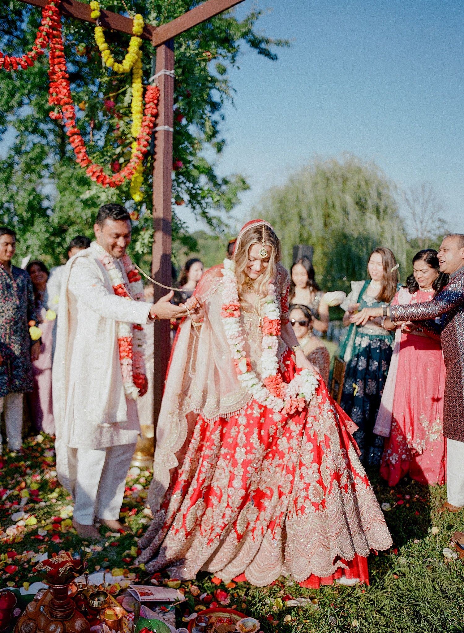 Festive outdoor celebration with decorative wooden arch adorned in vibrant red and yellow floral arrangements.