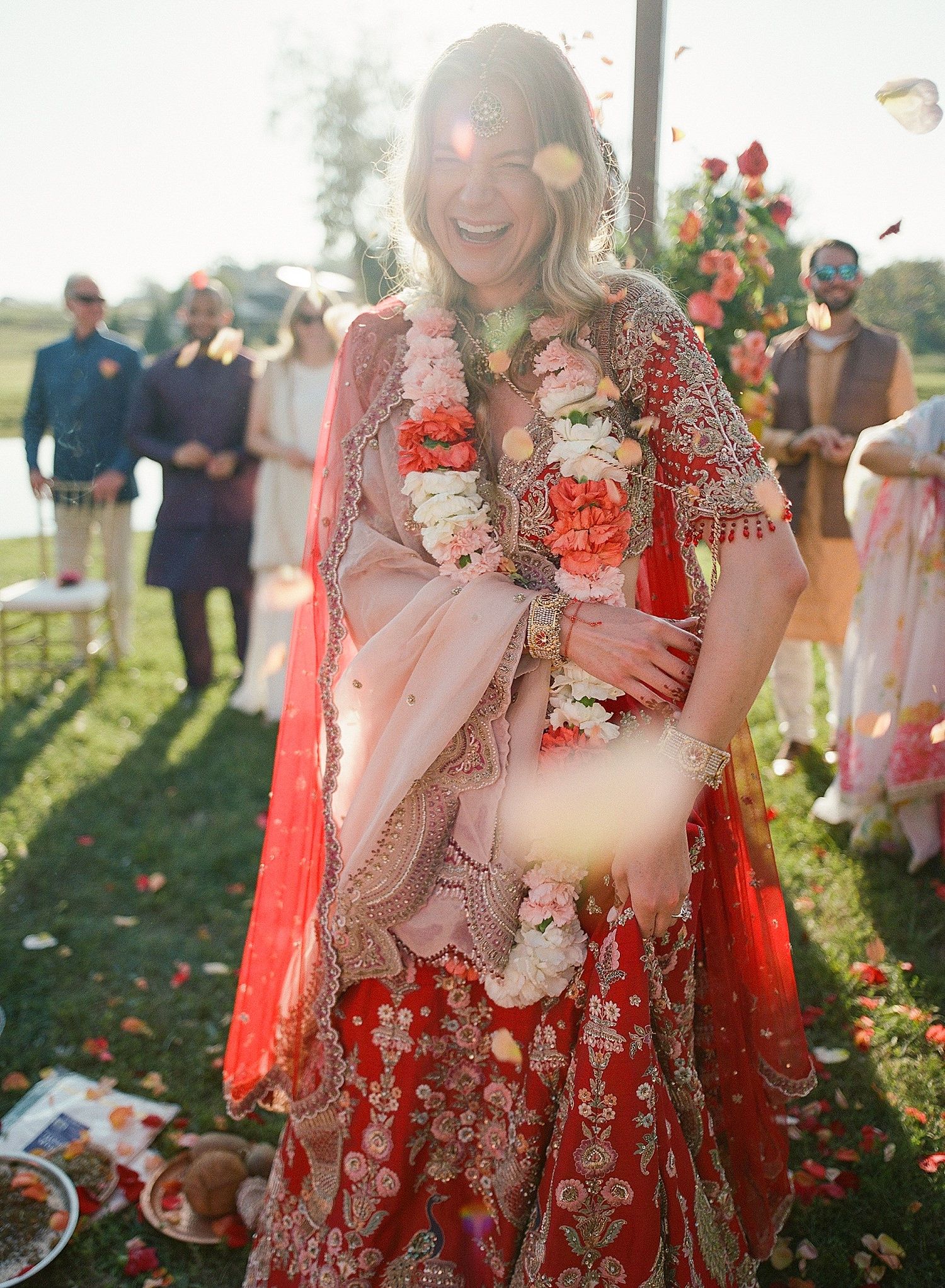 A wedding celebration in a garden setting with vibrant red traditional attire and floral decorations at sunset.