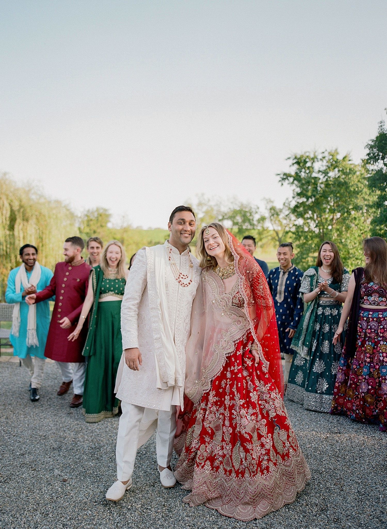 Wedding party in colorful formal attire walks along a gravel path during an outdoor celebration.