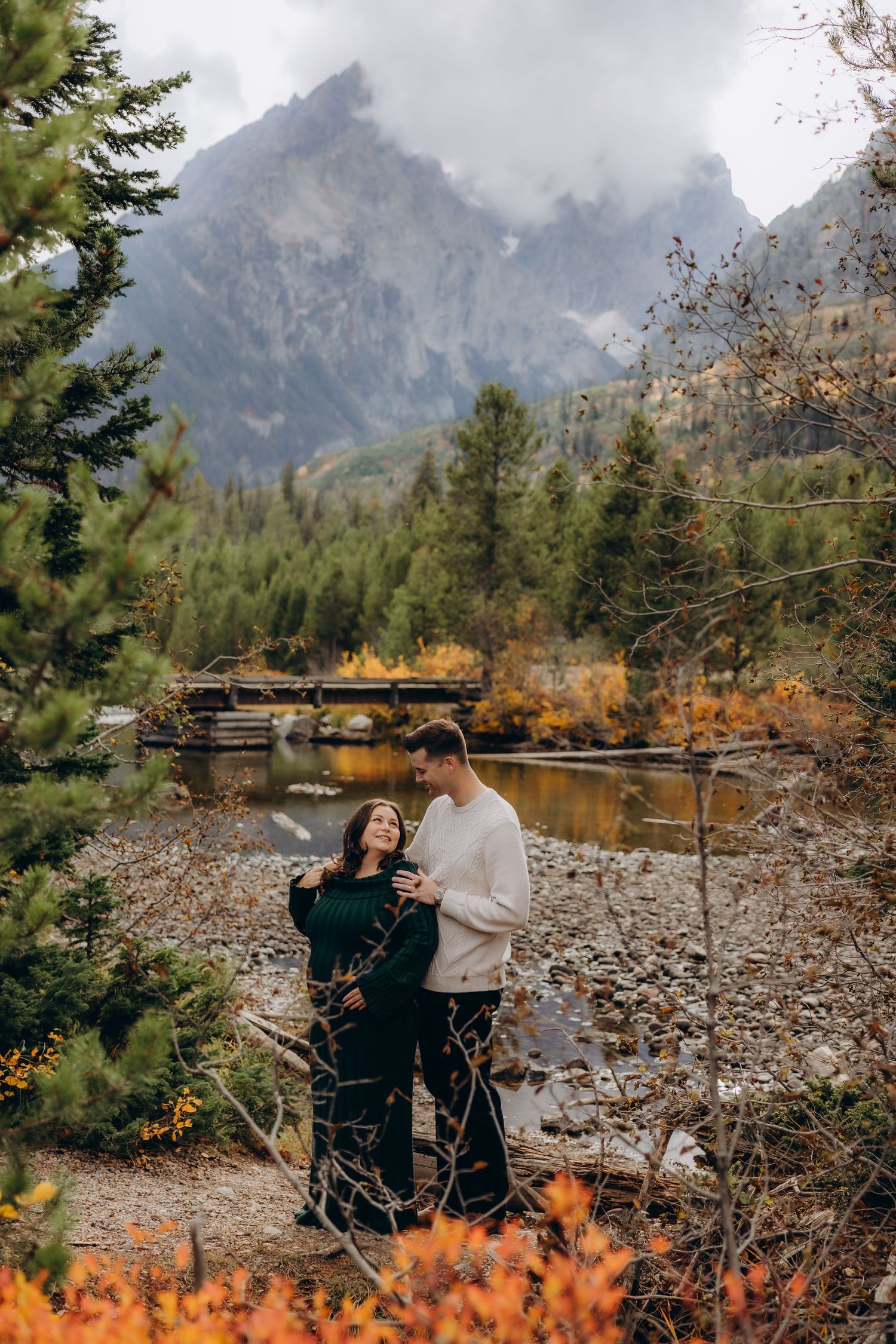 A couple shares a romantic moment against a backdrop of majestic mountains and autumn foliage in a scenic outdoor setting.