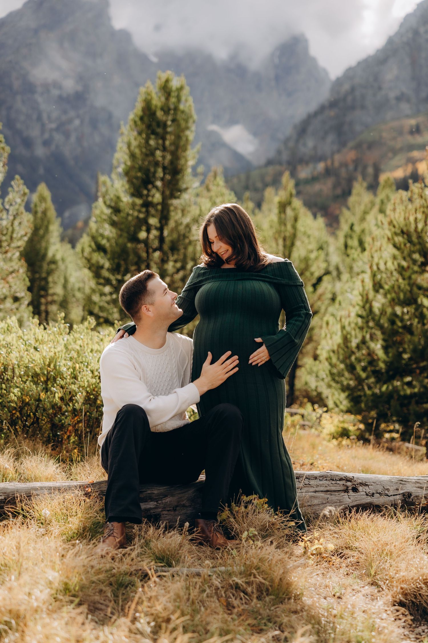 Candid moments between a couple relaxing on fallen logs with majestic mountain peaks and pine forests in the background.