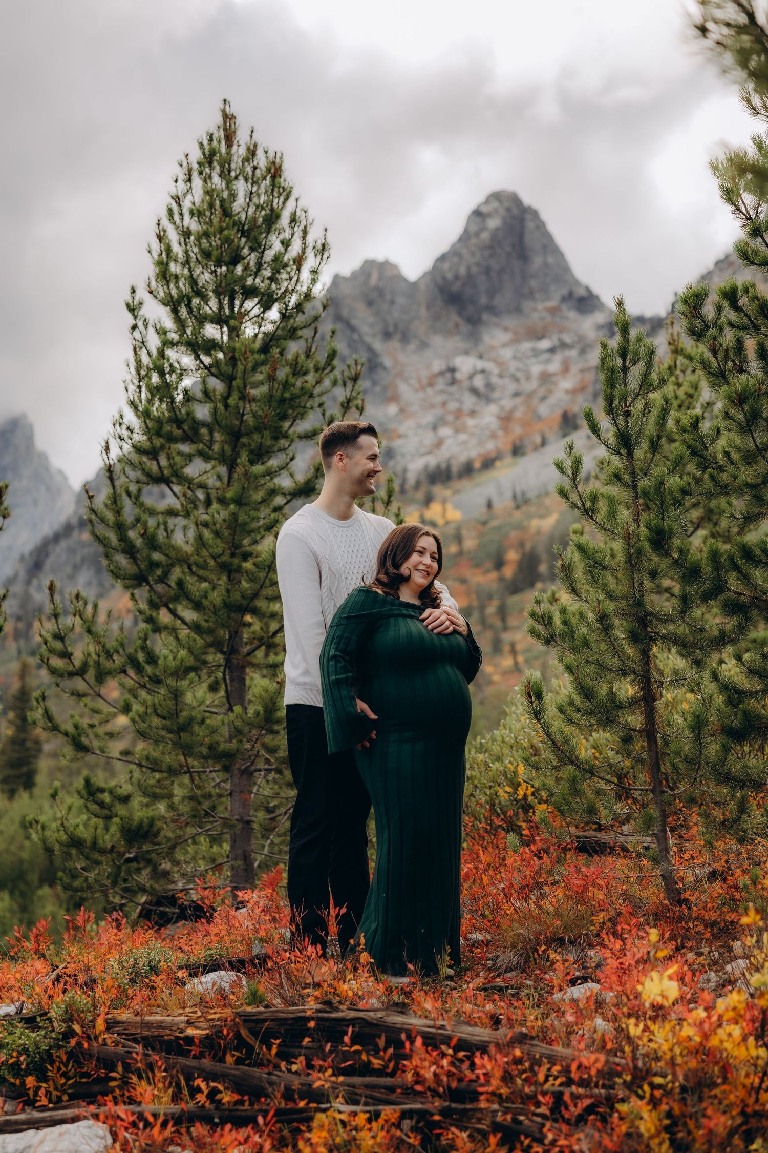 Couple enjoying an autumn day in the mountains with vibrant red foliage and evergreen trees against rocky peaks.