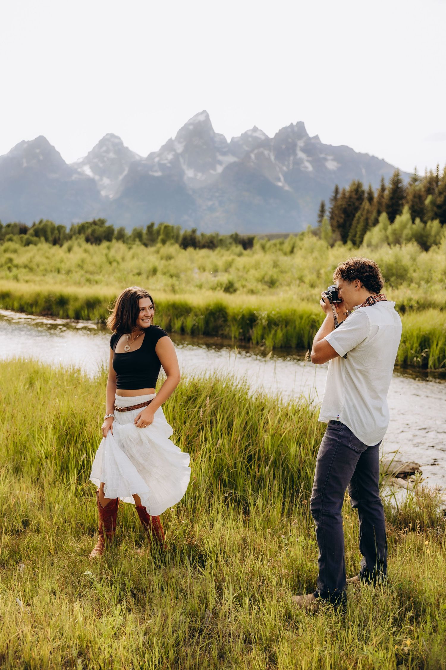 A couple dances playfully in a grassy meadow with majestic mountain peaks rising in the background.