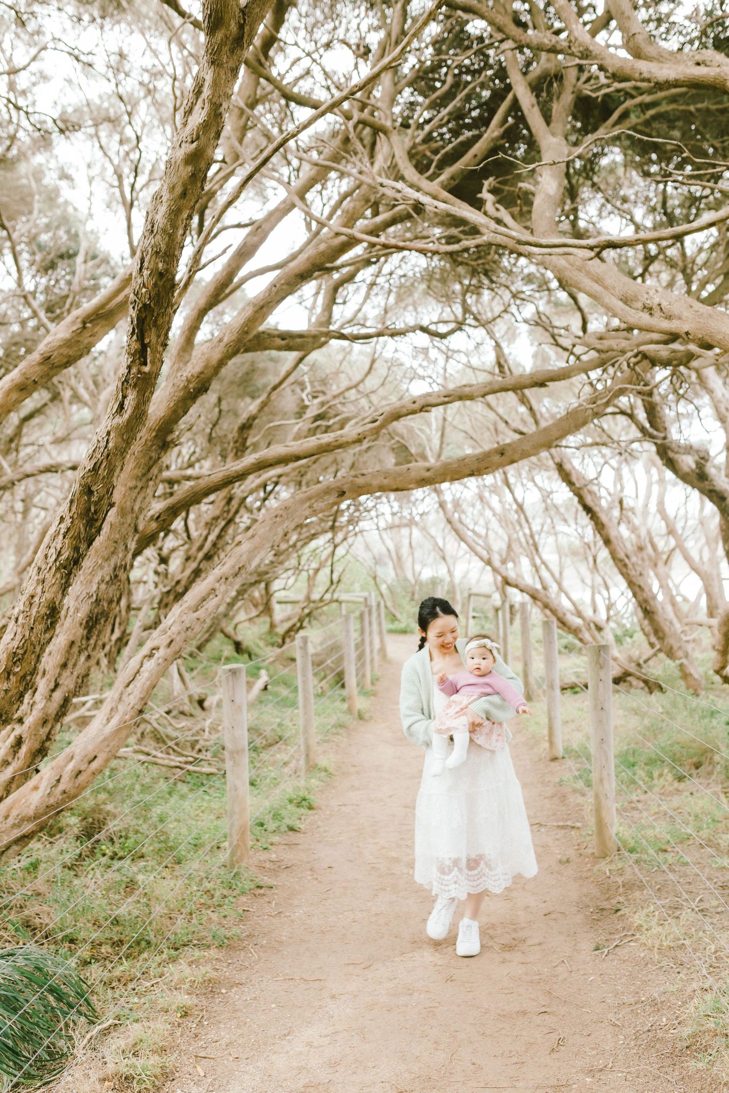 A romantic couple shares tender moments along a winding dirt path beneath twisted tree branches in a dreamy forest setting.