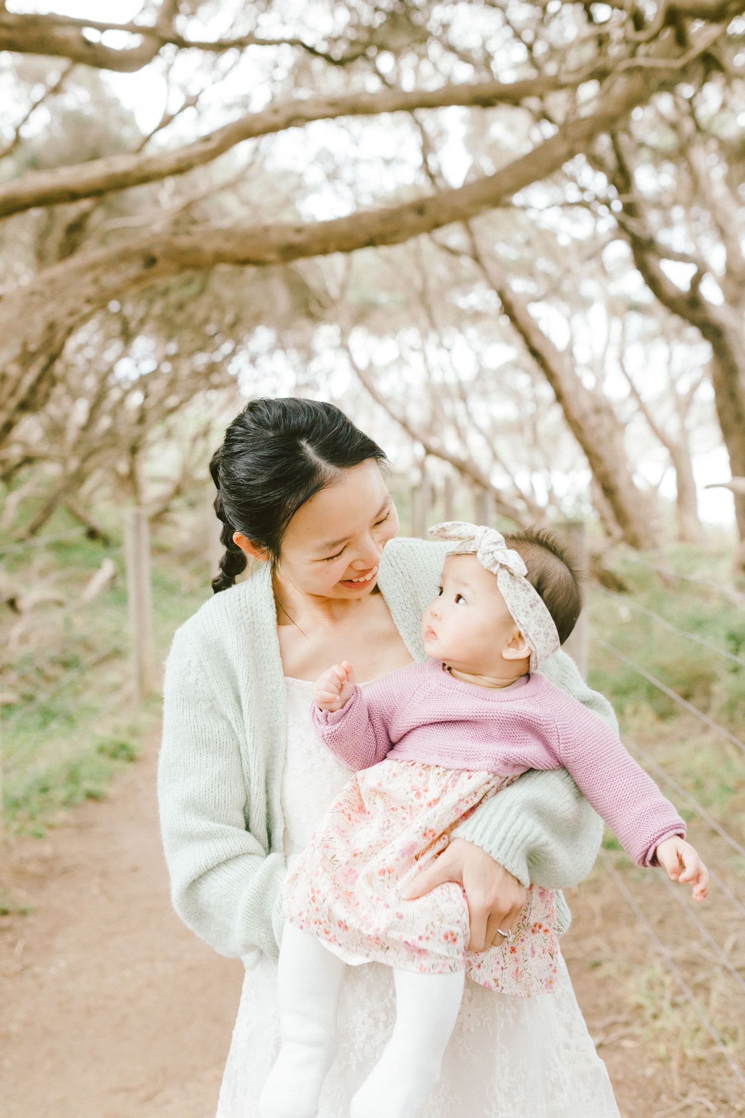 A tender moment between parent and baby in a soft outdoor setting with trees creating a dreamy natural backdrop.