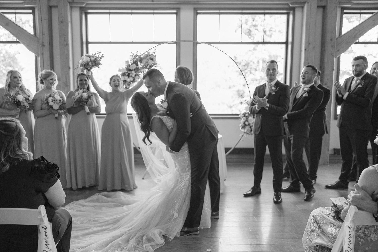 A couple shares their first dance surrounded by wedding party members in a bright venue.