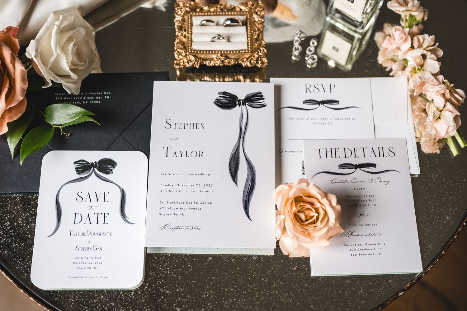 Black and white wedding invitations with elegant ribbon details and peach roses on dark surface.