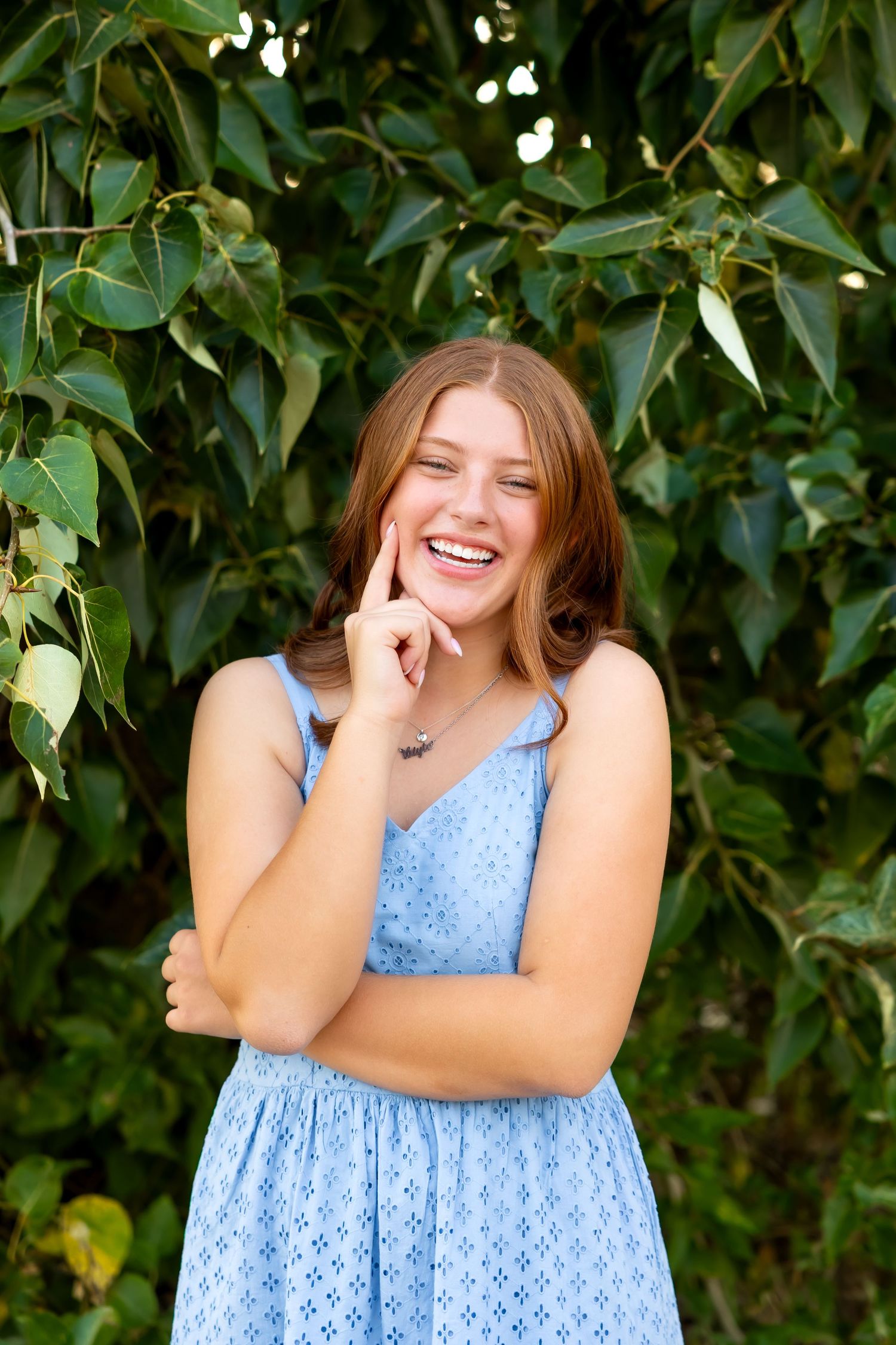 A light blue polka dot sundress contrasts beautifully with lush green foliage in a summer portrait session.