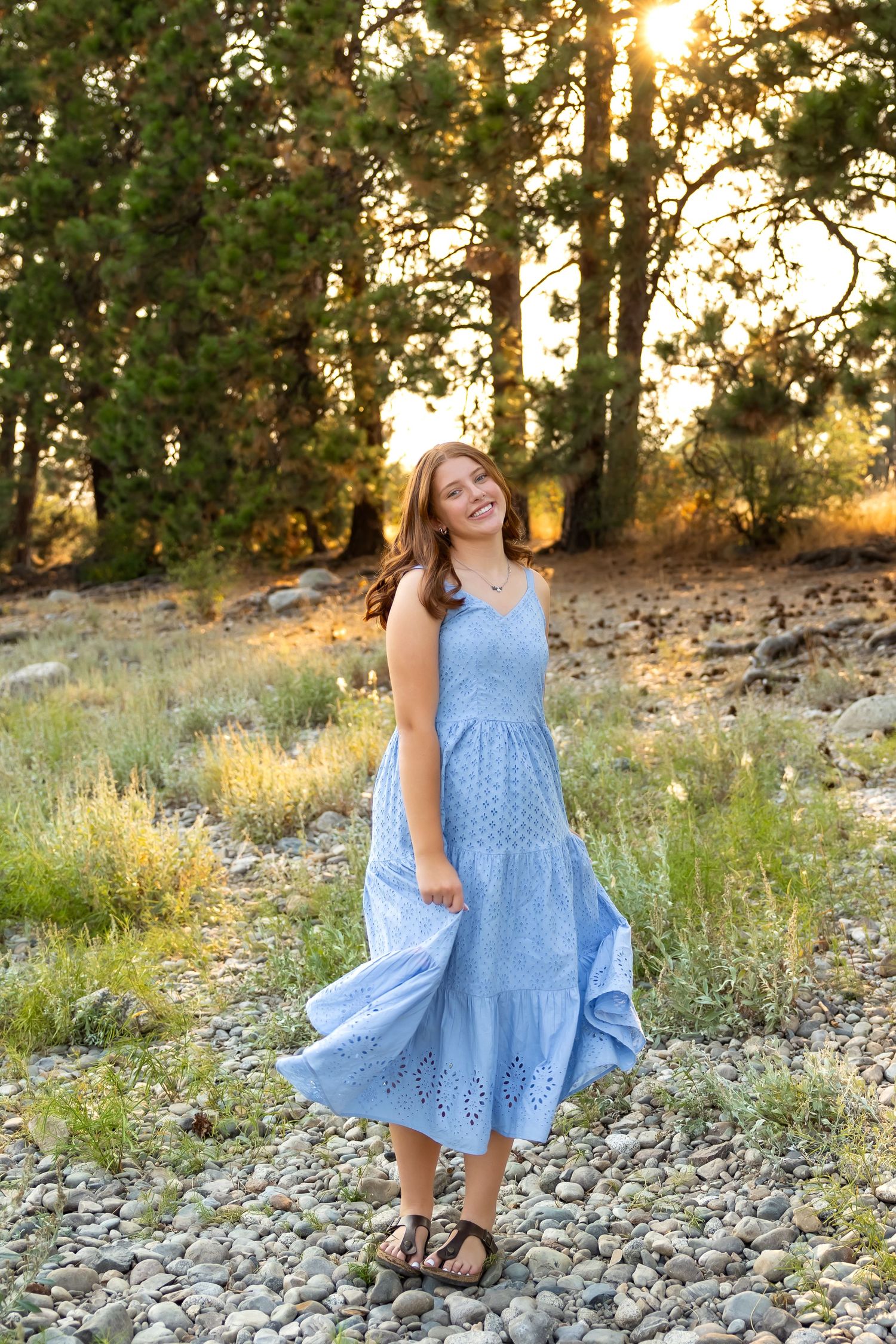 A light blue eyelet dress flows gracefully against a rocky landscape during golden hour sunset.