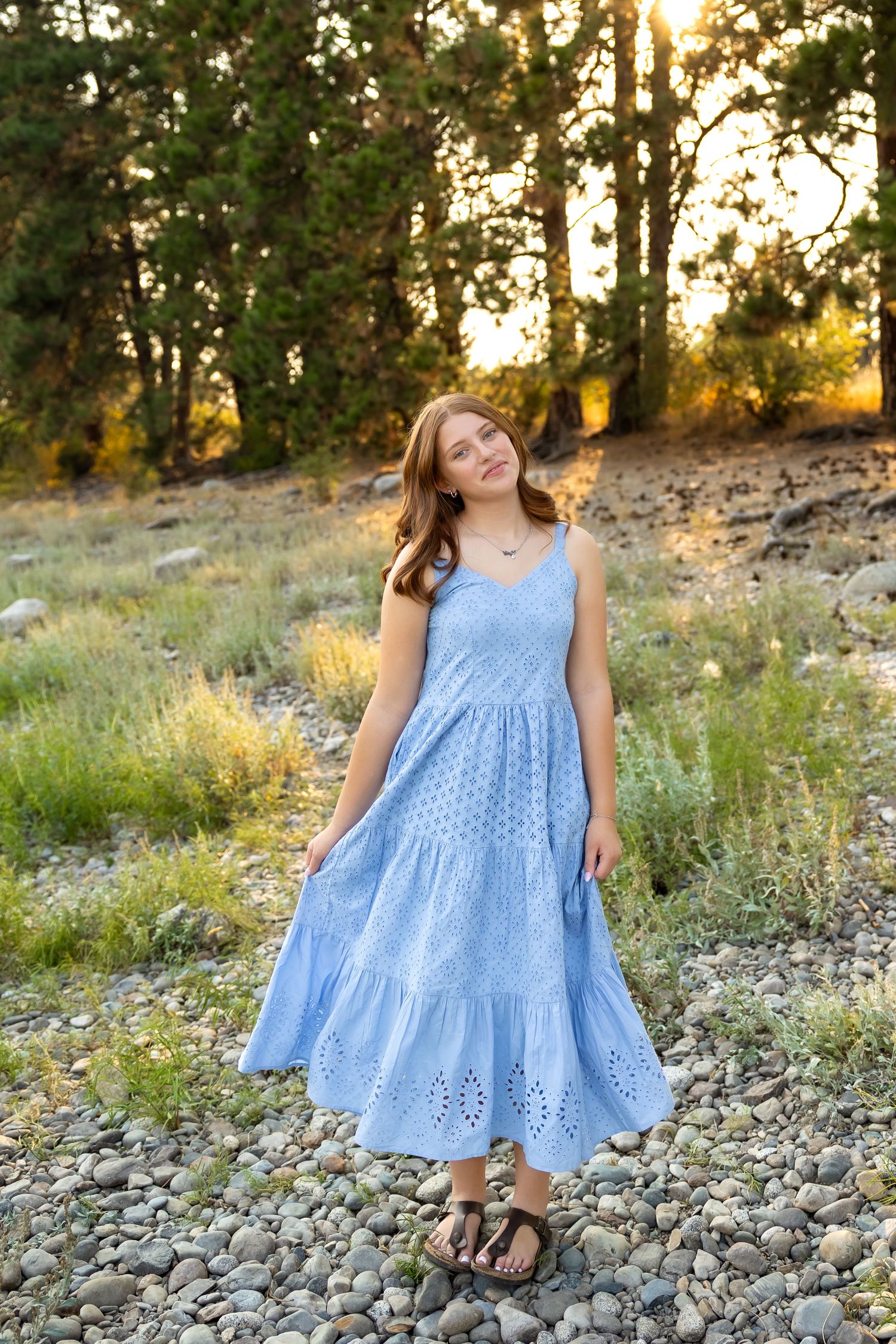 Person in flowing blue dress posing on rocky ground during golden hour sunset.